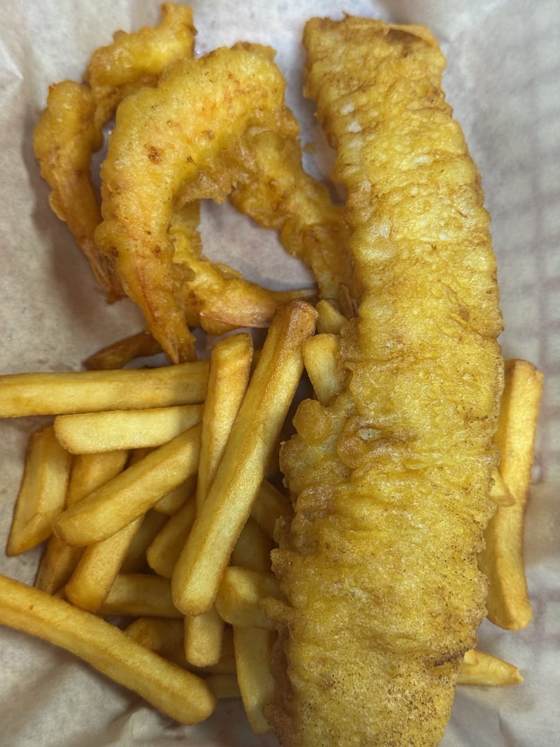 Golden-brown battered fish, fried shrimp, and french fries in a paper-lined basket.